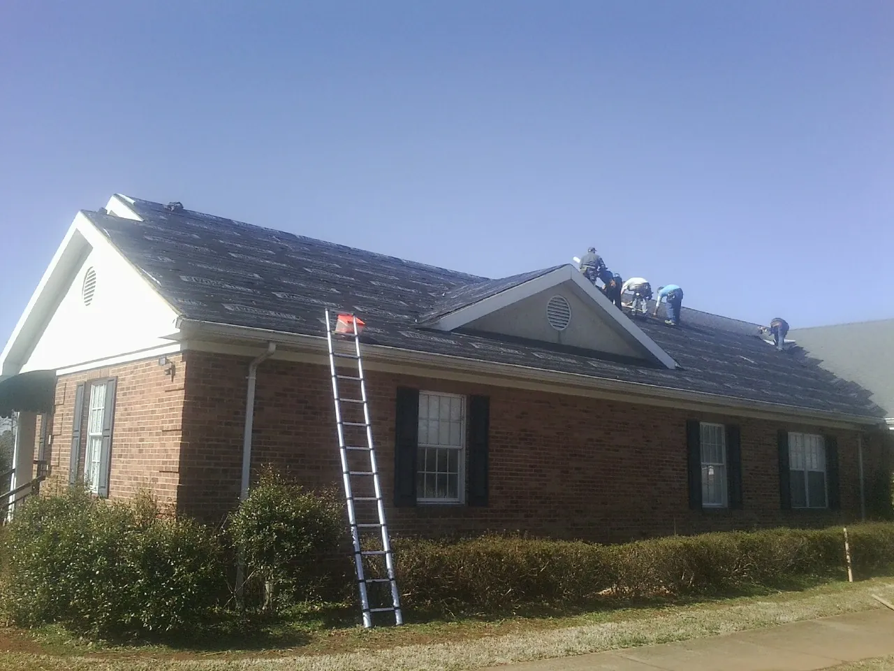 Crew tearing shingles off a brick ranch roof with a ladder set — Emergency Roof Repair work by our crew in Whitehall