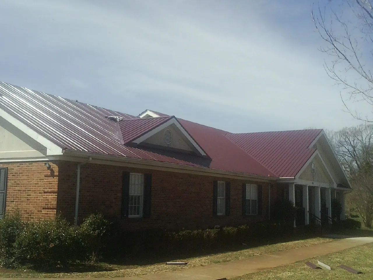 Red metal roof with gabled entries on a long brick building, from a Hail Damage Roof Repair job in Whitehall
