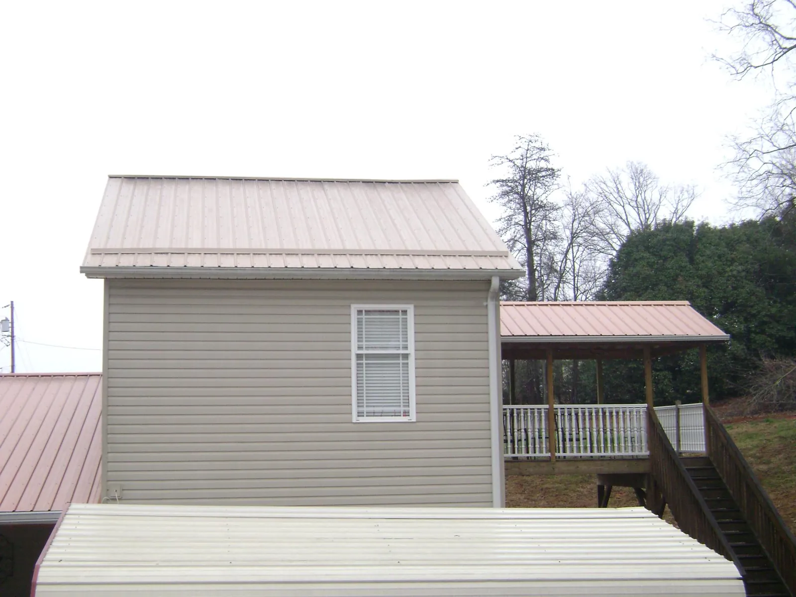 Tan metal roofs on a two story addition and attached porch, from a Roof Replacement job in Whitehall